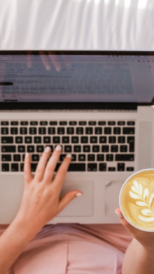 person using MacBook Pro and holding cappuccino